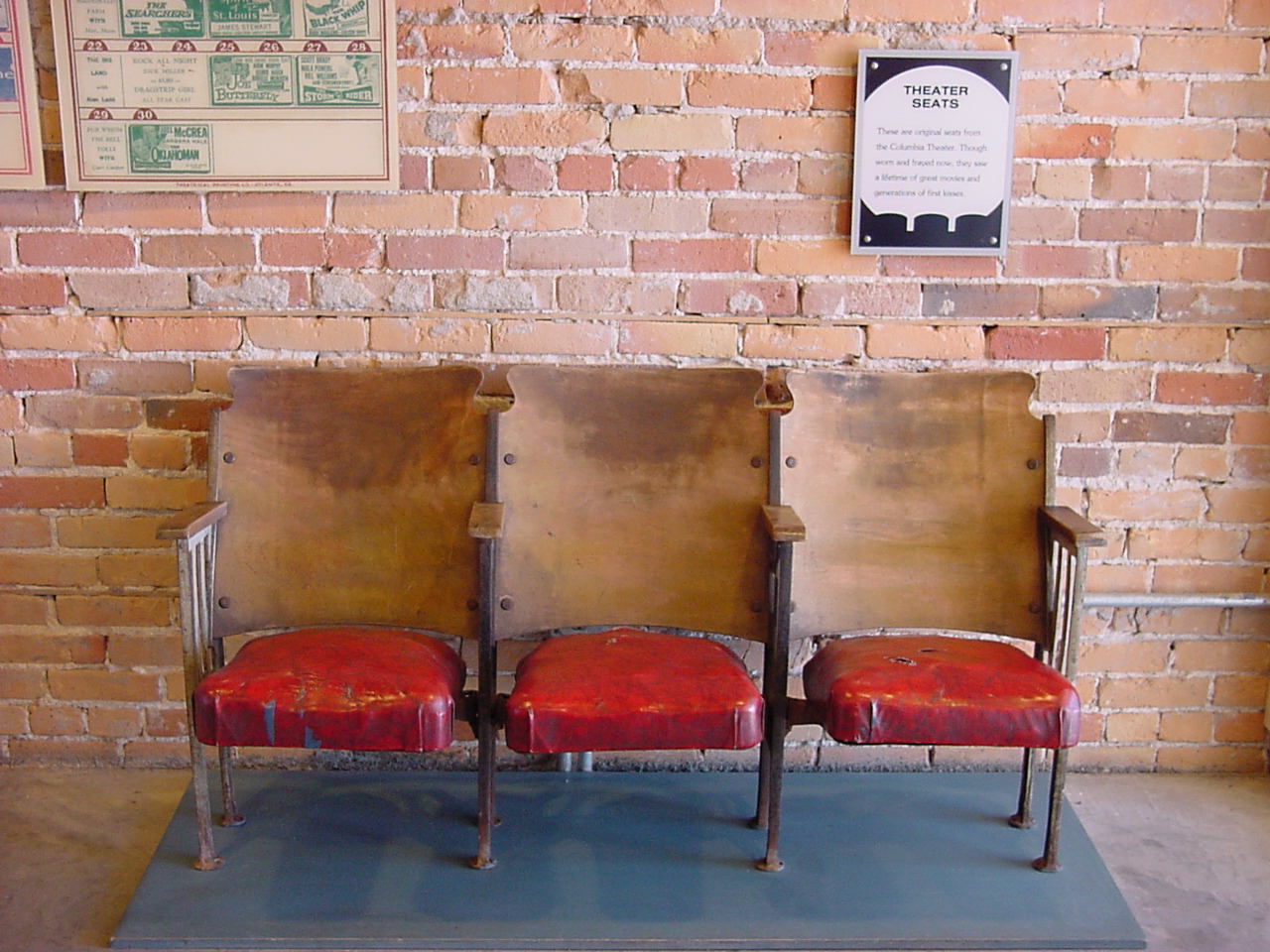Three worn wooden theater seats in a row inside an old cinema.