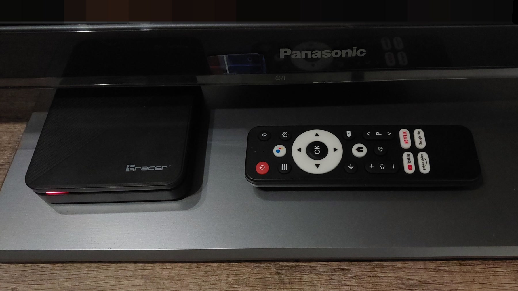 A Tracer Android TV set-top box and its remote in front of a Panasonic television.