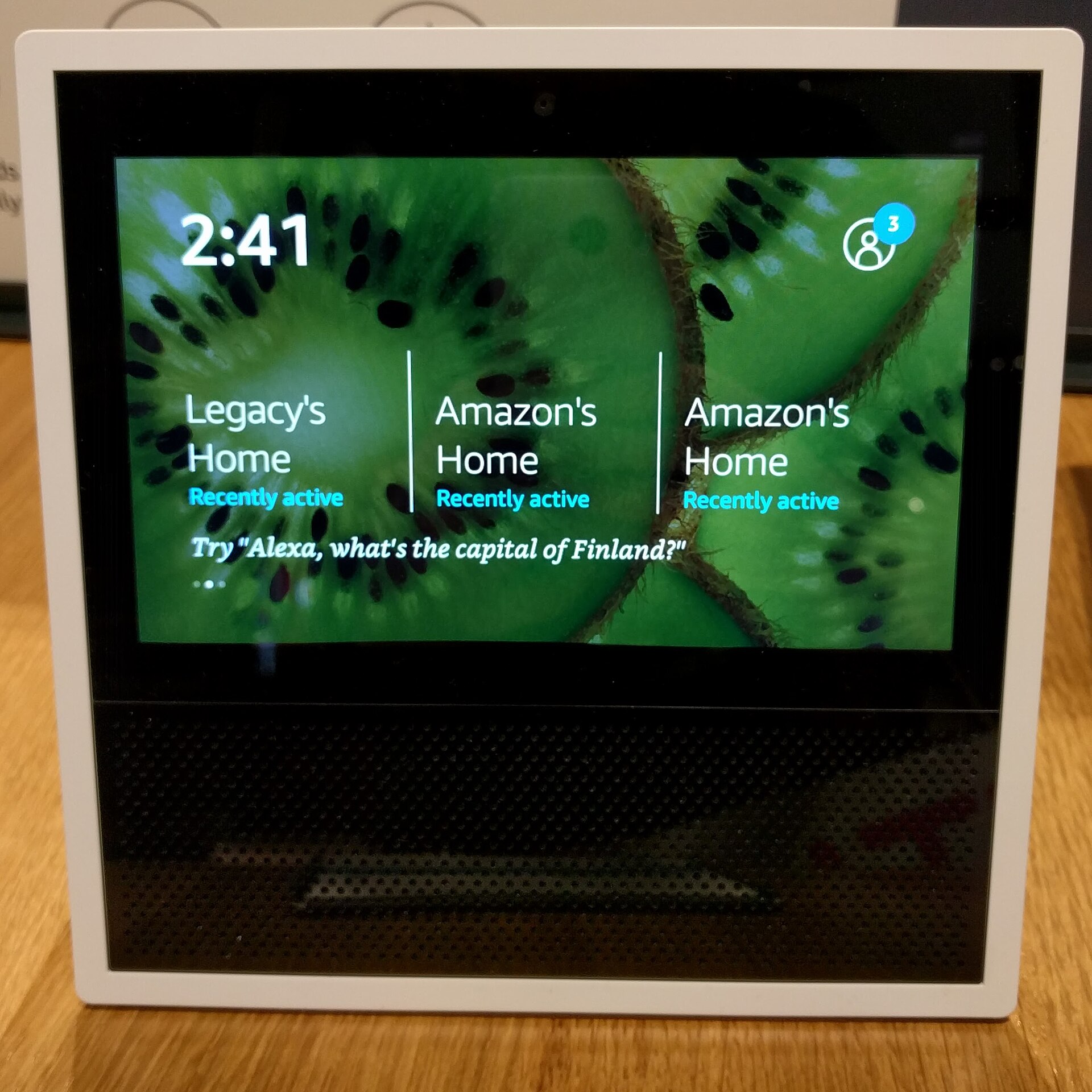 A white Amazon Echo Show smart display on a white background, its screen showing a nature photo of a canyon and a river.
