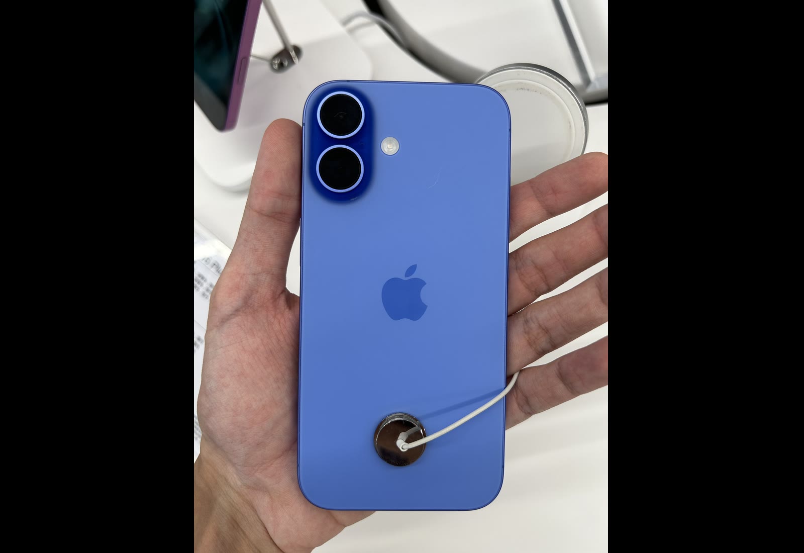 The back of an ultramarine iPhone 16, an earlier iPhone, on a black background, showing the camera module and Apple logo.