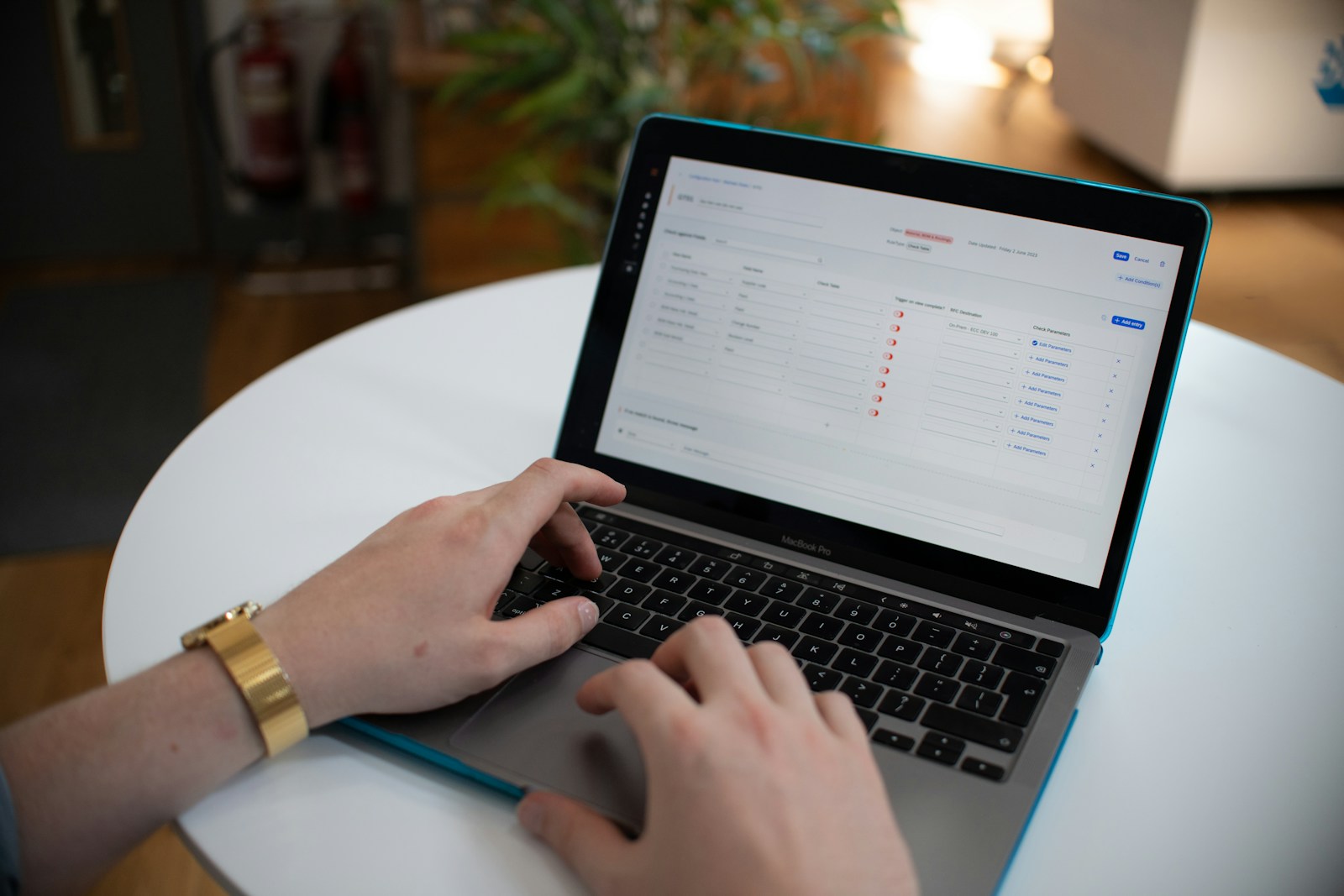 Hands using a laptop displaying rows of editable form fields on a white table.