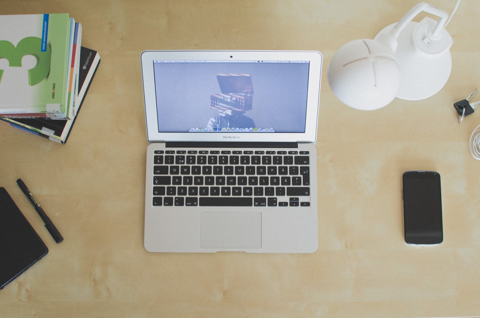 An overhead view of a silver laptop on a wooden desk beside a phone, books and white headphones.