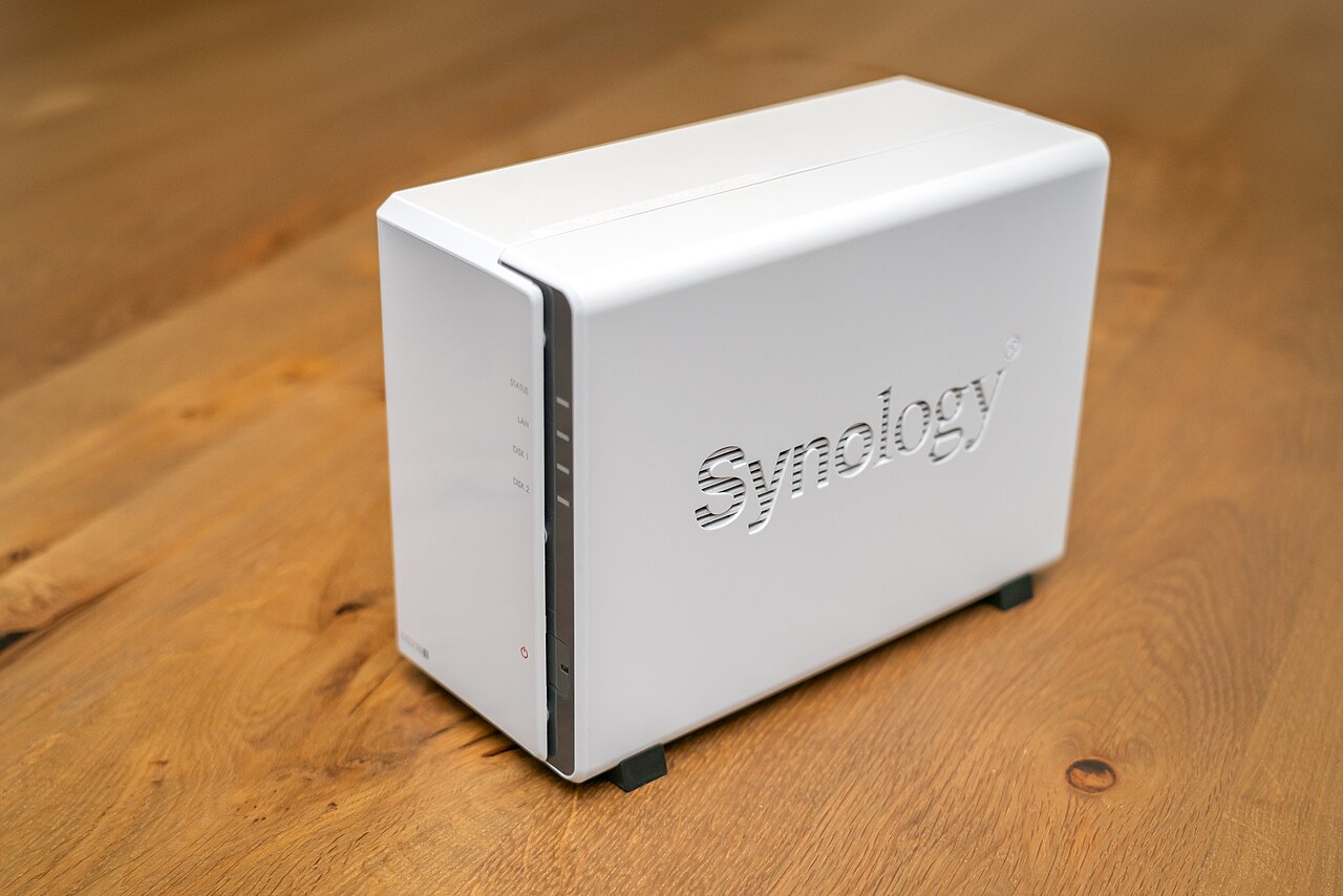A white Synology network-attached storage enclosure standing on a wooden floor.