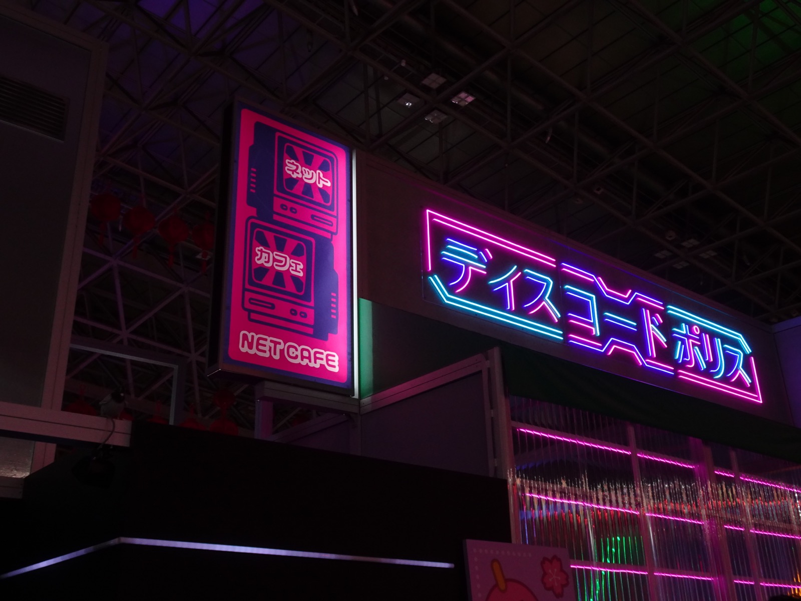 Pink and blue neon Japanese signage above Discord’s booth inside an exhibition hall.