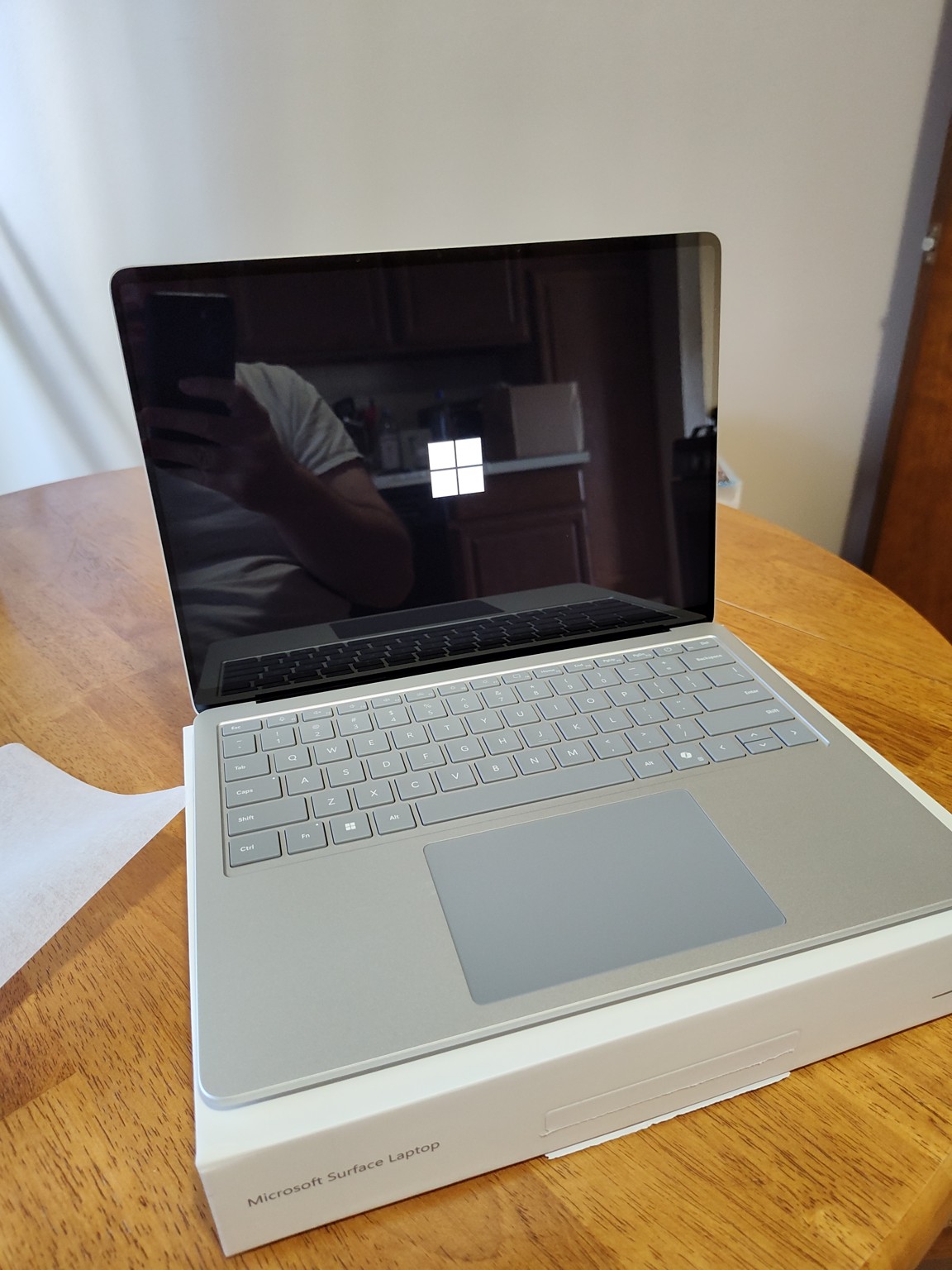 A silver Surface Laptop 7 showing the Windows boot logo, resting on its box on a wooden table.