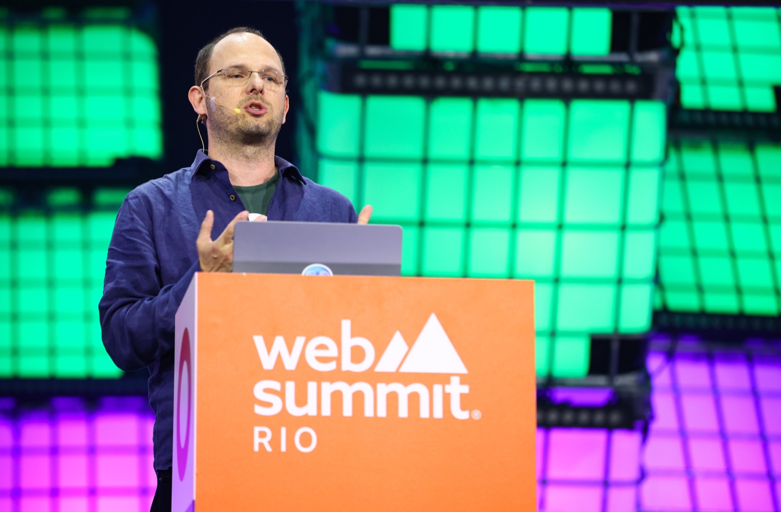 Thomas Dohmke speaking behind a Web Summit Rio lectern with a laptop and a green-lit backdrop.