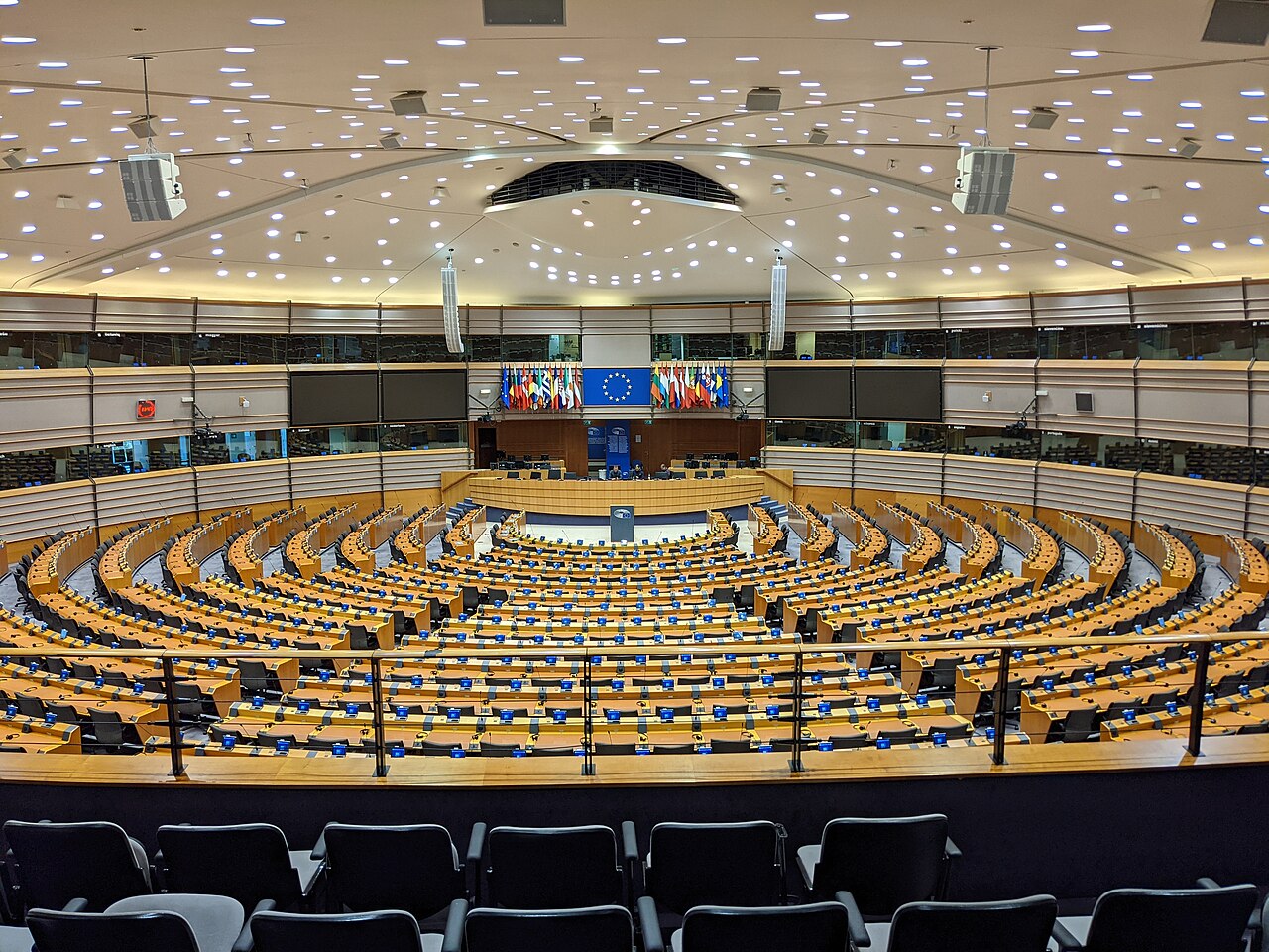 The European Parliament hemicycle in Brussels, with curved rows of blue seats facing a central podium.