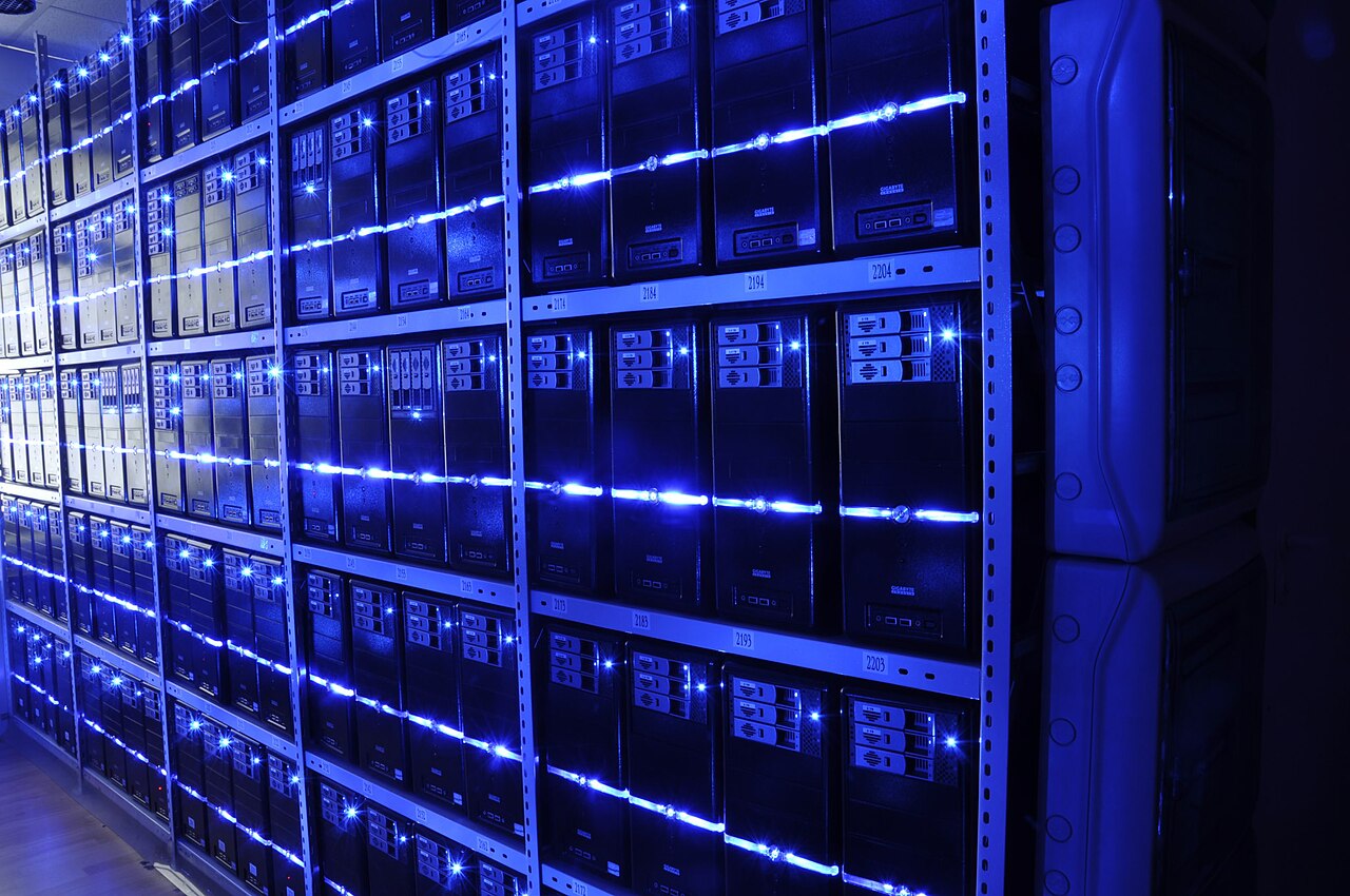 Rows of black server racks in a data centre aisle, lit with blue light.