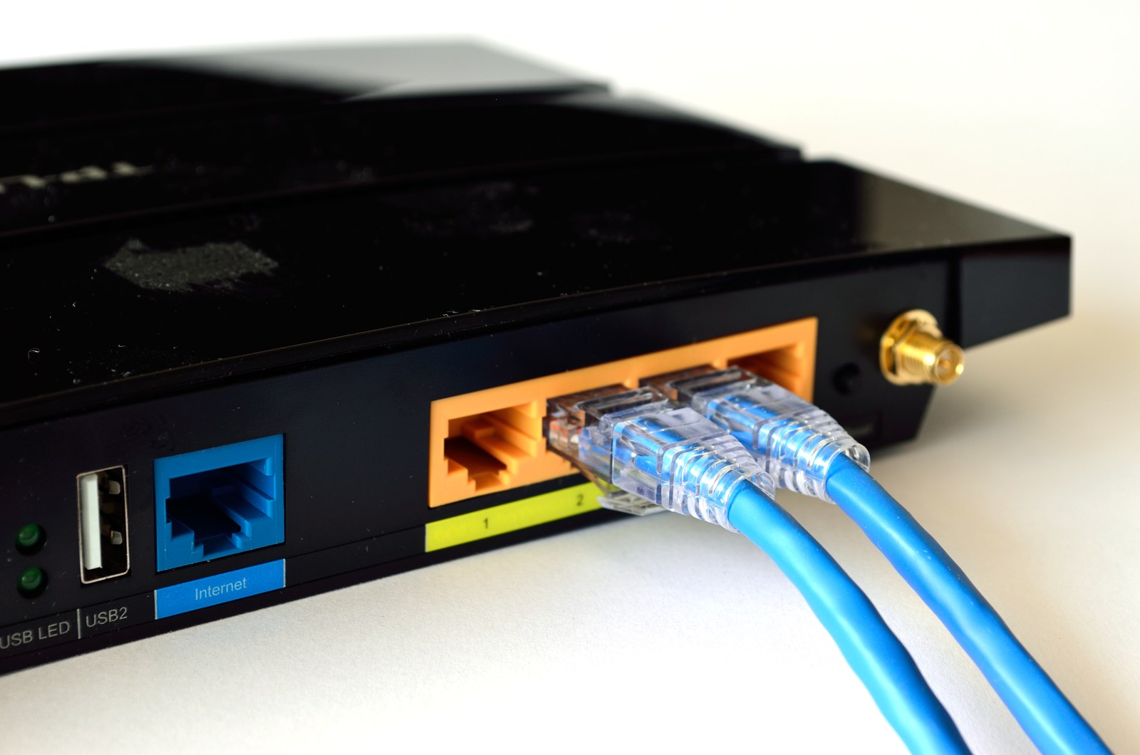 Two blue Ethernet cables plugged into yellow ports on the back of a black Wi-Fi router.