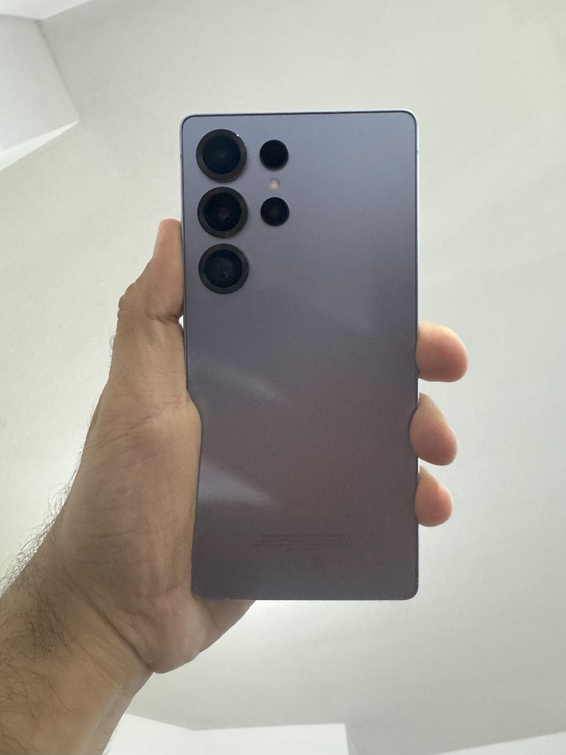A hand holds a gray Samsung Galaxy phone with its rear camera lenses facing the viewer.