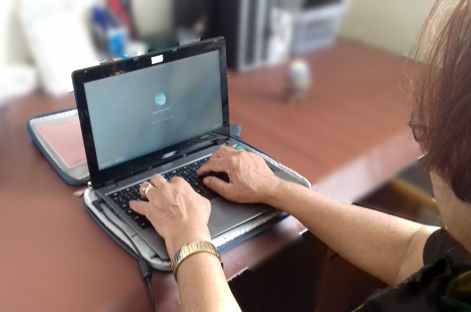 A person typing on a Chromebook resting in an open carrying case on a table.