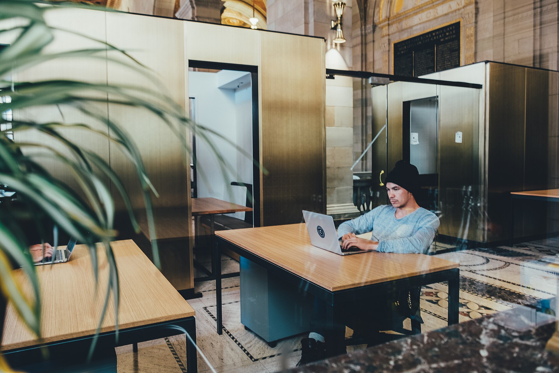 Rows of desks with laptops in a bright open office, with people working.