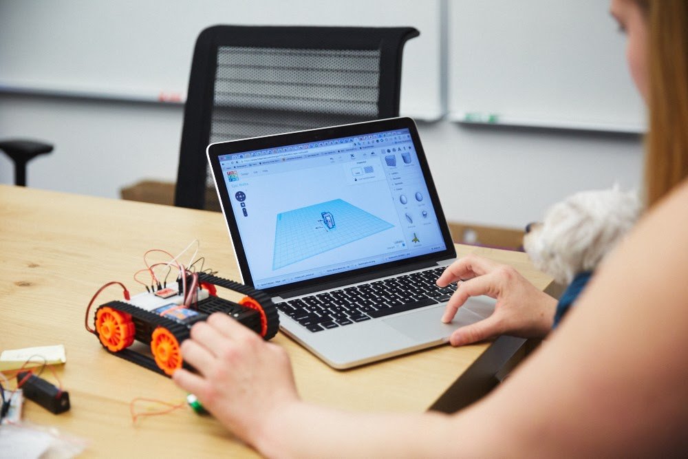 A Google employee works with a laptop and a small wheeled robot in an office.