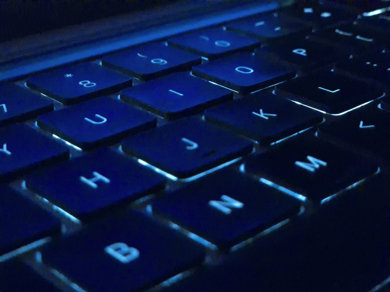 Close-up of a MacBook Pro's black keyboard illuminated by blue light.