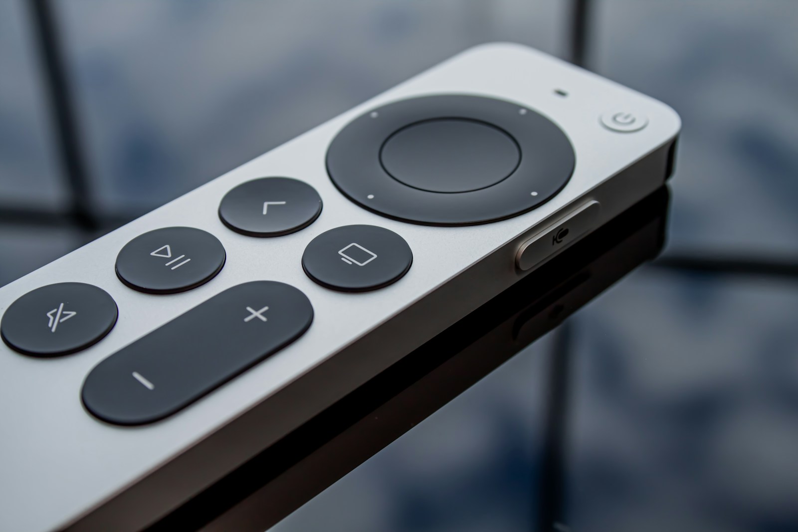 Close-up of a silver Apple TV remote with a black circular clickpad and playback buttons.