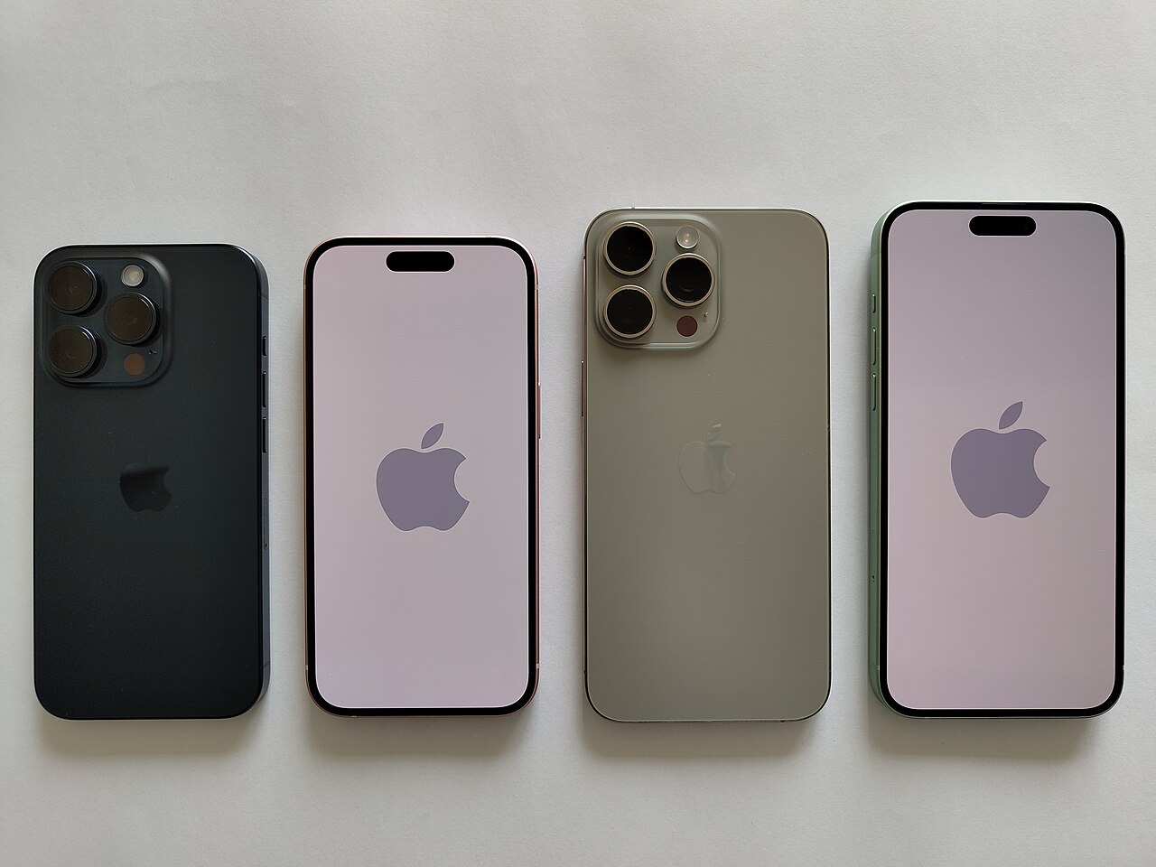 Four iPhones arranged on a pale surface, showing two backs and two screens with Apple logos.