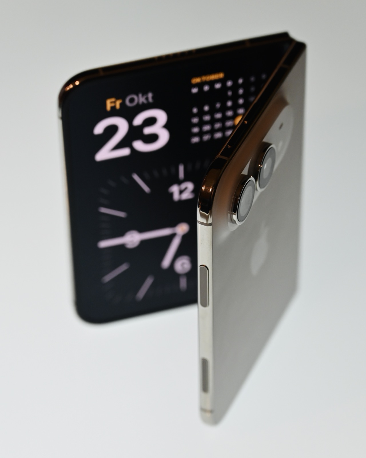 A partially folded white iPhone Duo standing upright, with a clock on its screen and its rear cameras visible.