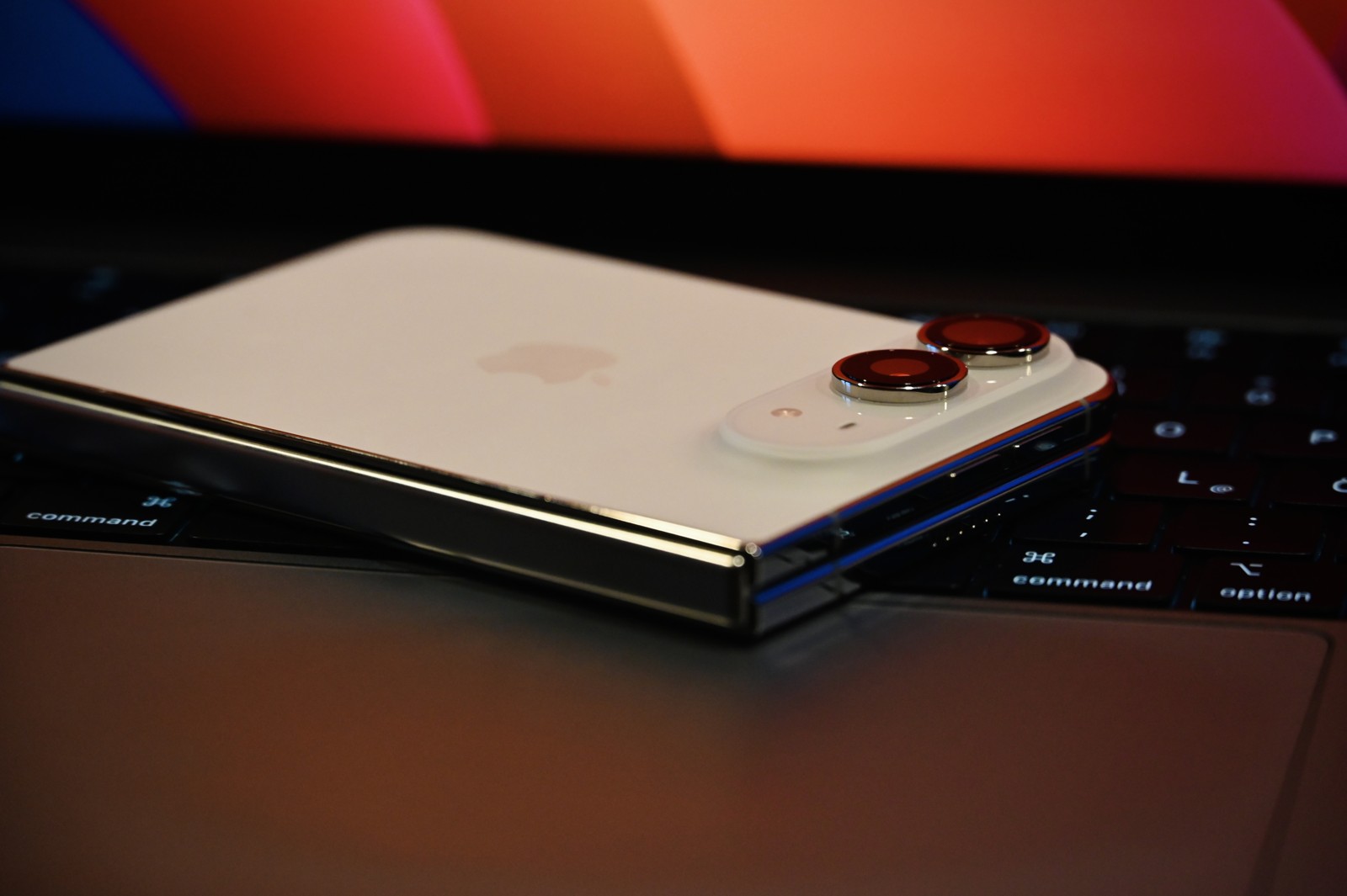 A folded white iPhone Duo resting rear-side up on a laptop keyboard, with its cameras and folded edge visible.