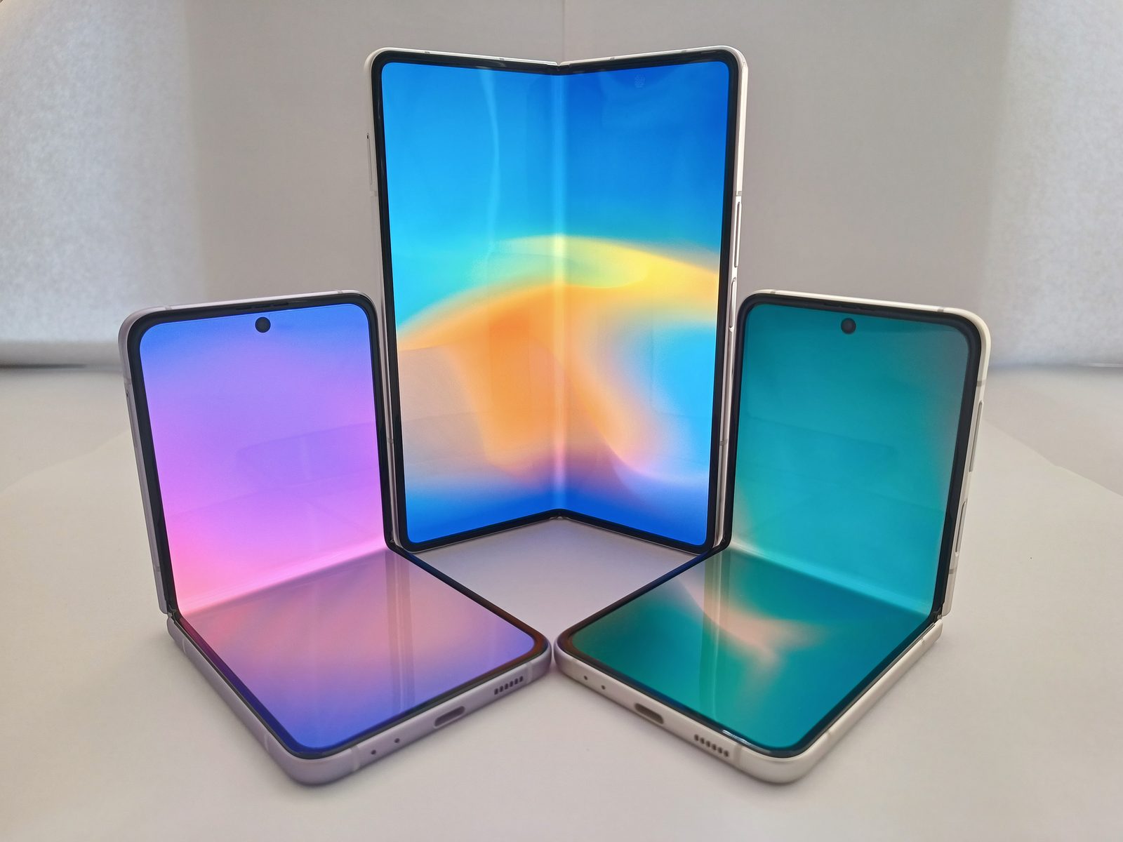 A Samsung Galaxy Z Fold and a Samsung Galaxy Z Flip on a white surface, one partly open and one lying flat.