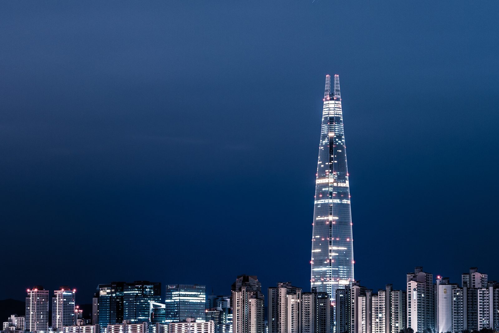 Seoul's skyline at night across the Han River, with illuminated towers and bridge lights reflected on the water.