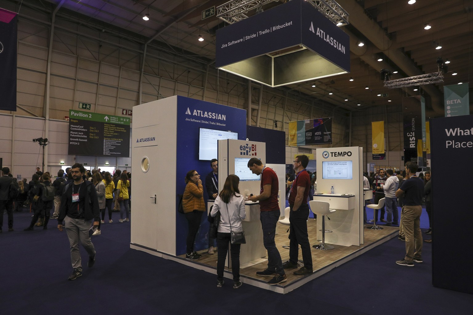 Visitors gather around Atlassian's blue-and-white stand beneath a suspended sign at Web Summit in Lisbon.
