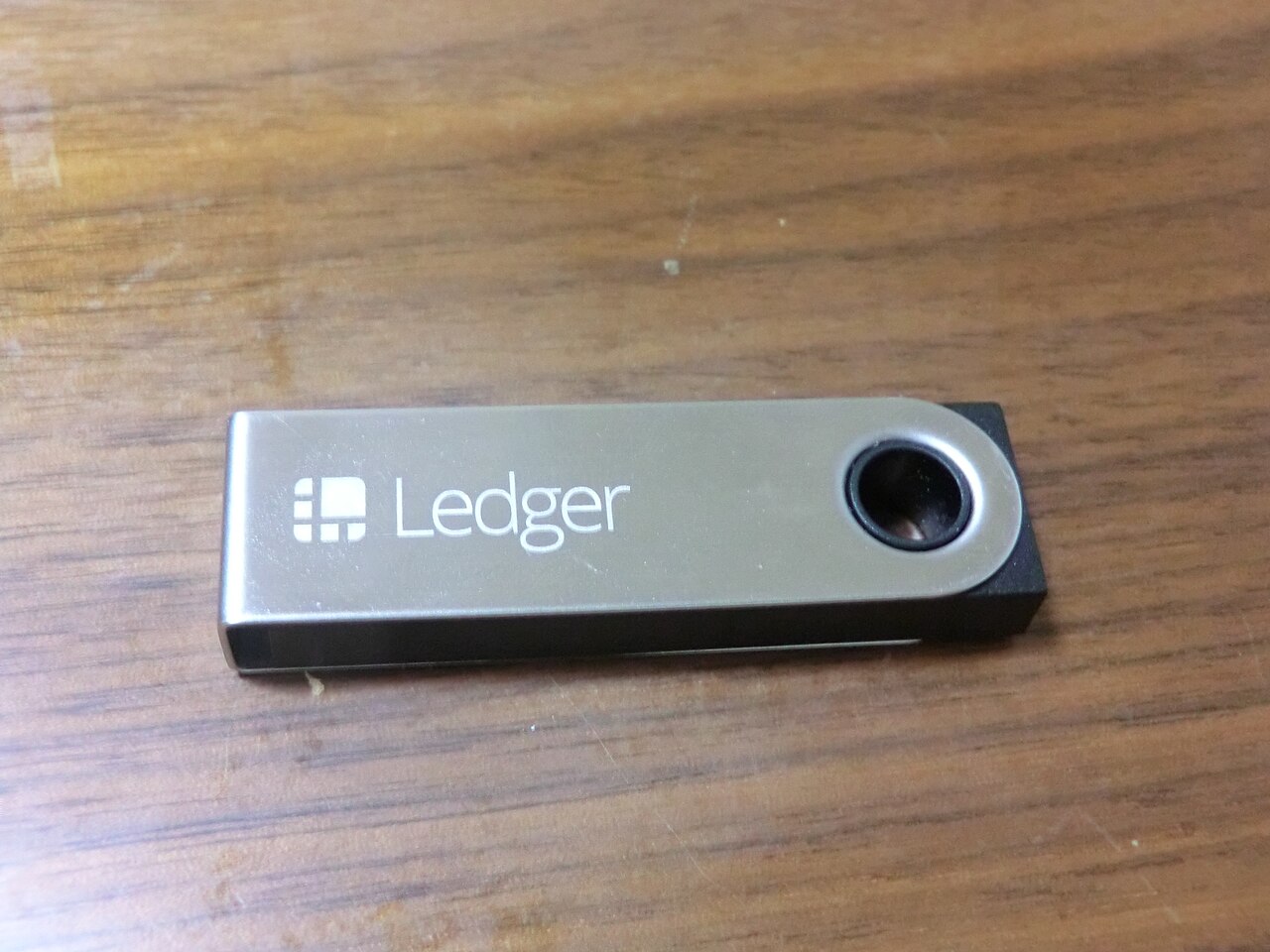 A Ledger Nano S hardware wallet with a USB cable on a wooden desk.