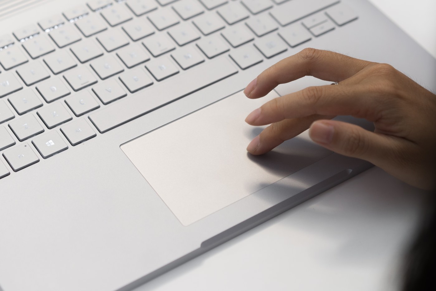 A hand using the touchpad of a silver Microsoft Surface Book 2, beside its keyboard.