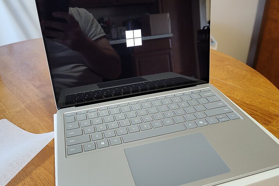 A silver Microsoft Surface Laptop 7 on a wooden table, with the Windows logo visible during startup.