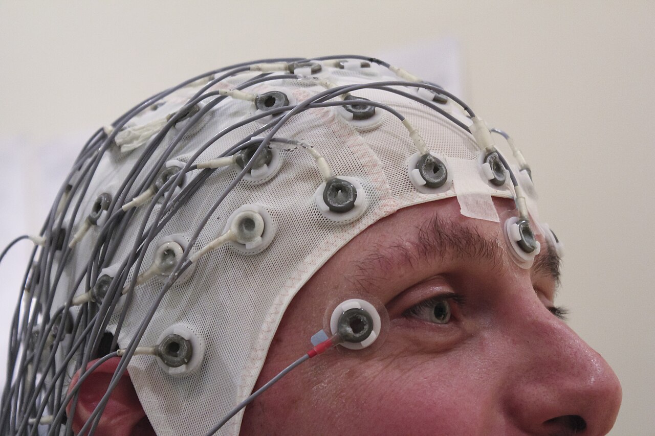 A person wearing a blue EEG cap covered in electrodes, with wires running off to the side.
