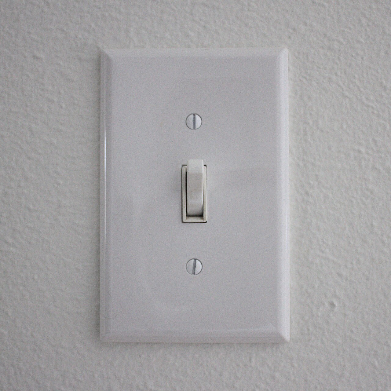 A white physical toggle light switch mounted on a textured white wall.