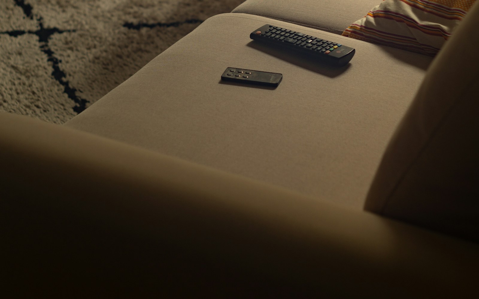 Two black remote controls rest on a beige sofa beside a striped cushion.