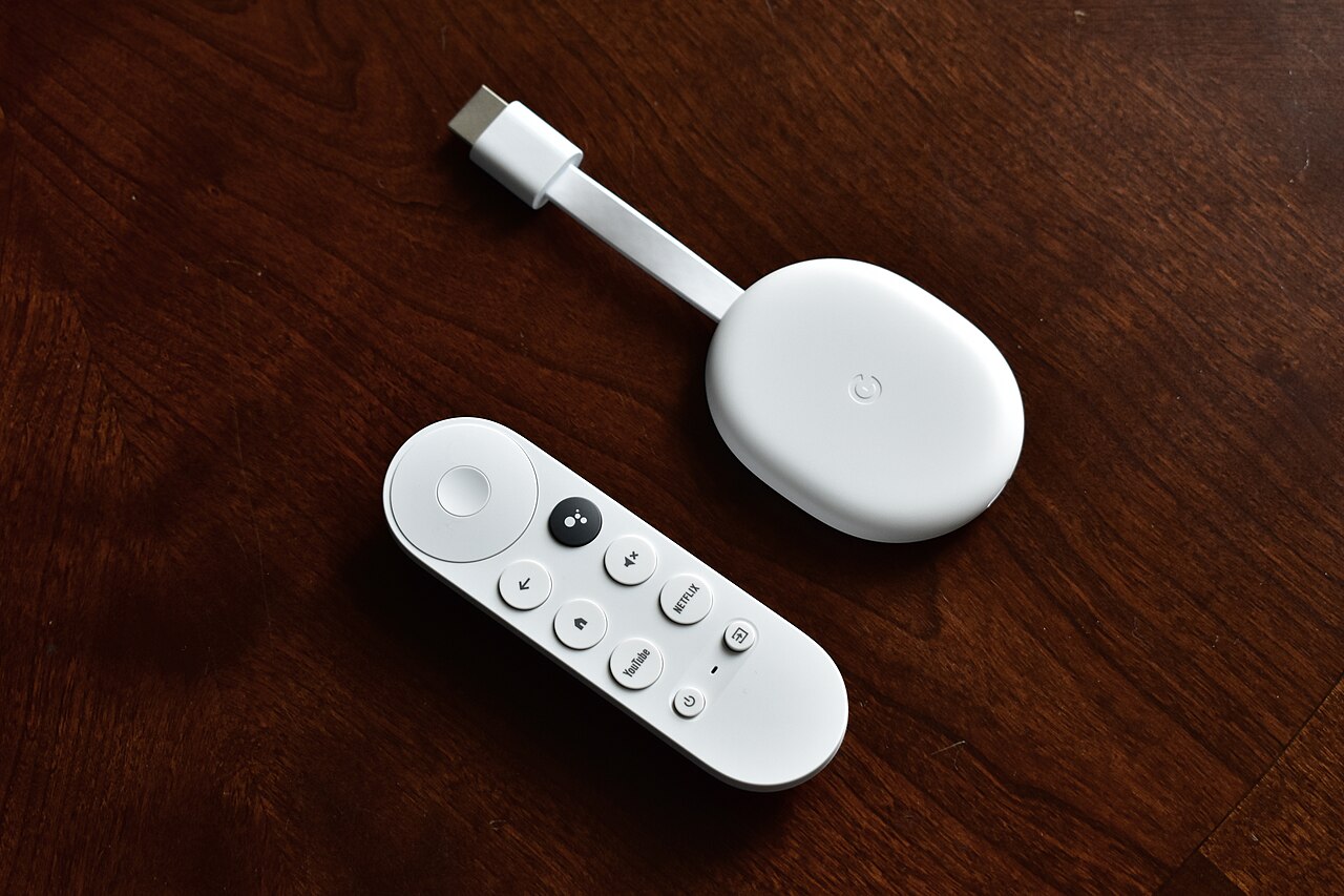 A white Chromecast with Google TV and its remote control on a wooden table.