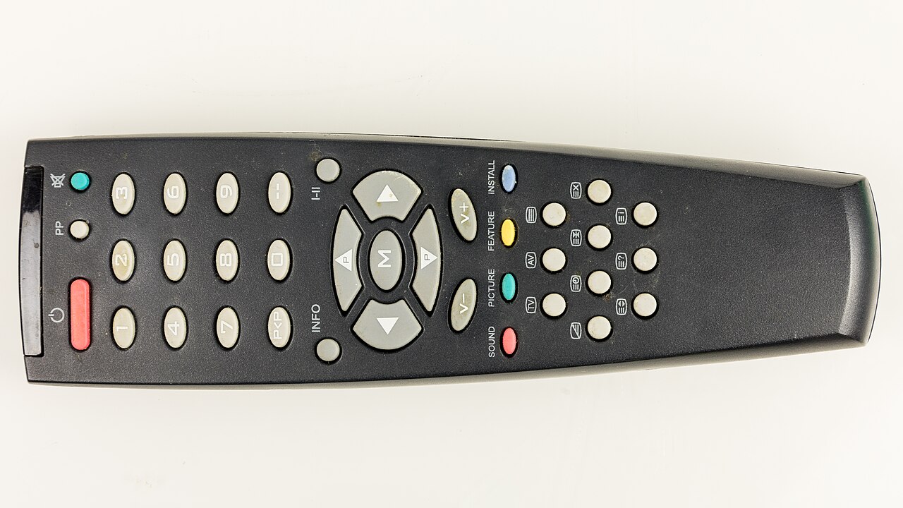 A black television remote with numbered keys and coloured buttons on a light background.