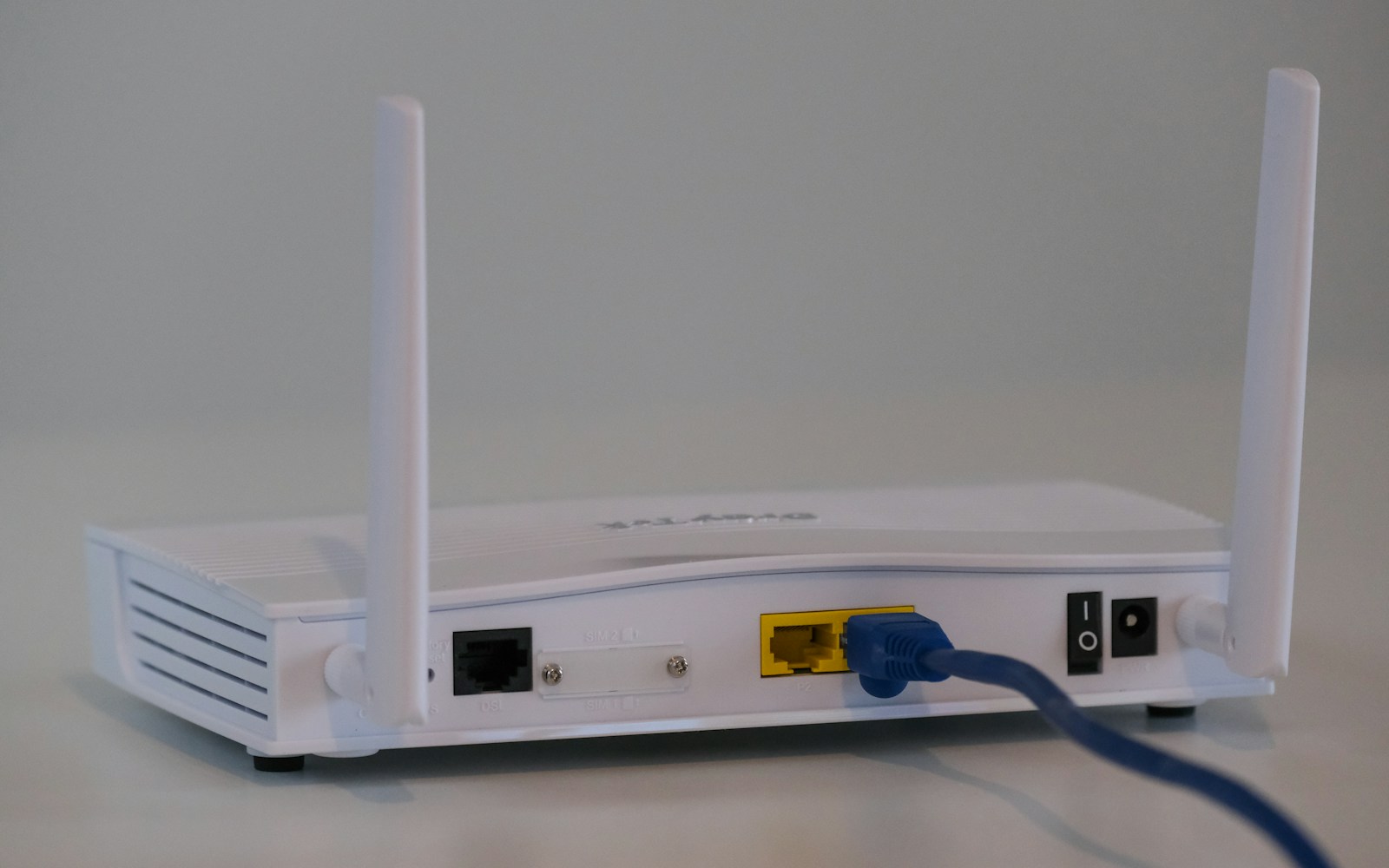 Rear of a white wireless router with two antennas and a blue Ethernet cable plugged into a yellow port.