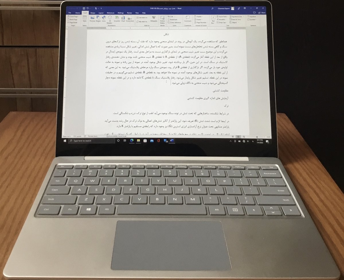 A silver Surface Laptop Go on a wooden desk displays a document in Microsoft Word.