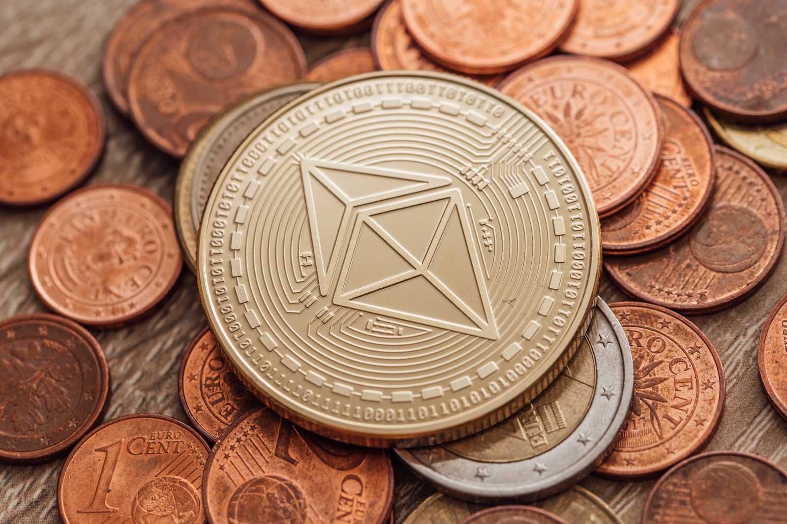A physical Ethereum coin held in a hand above a pile of ordinary metal coins.