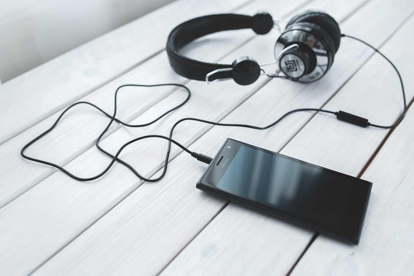 Wired over-ear headphones connected to a Nokia smartphone on a white wooden table.