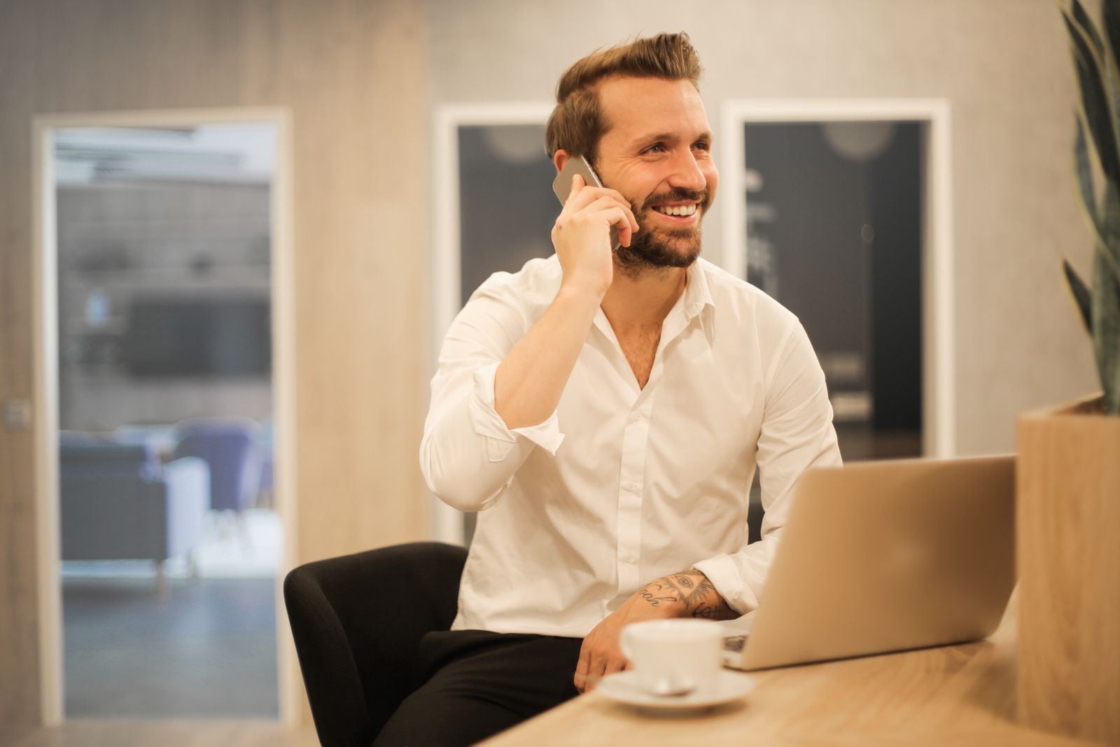 Smiling man in an office talking on a smartphone with a laptop open