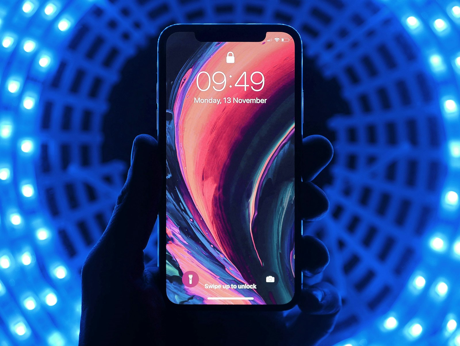 Hand holding an iPhone with a colorful lock screen against blue LED lights