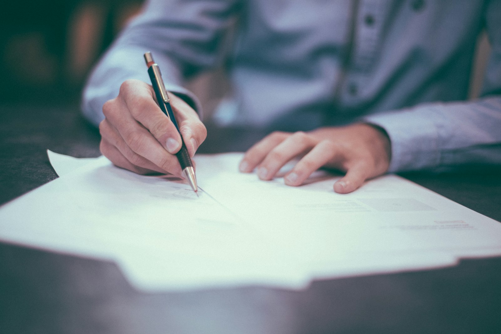 Hands signing a contract with a pen on a wooden desk