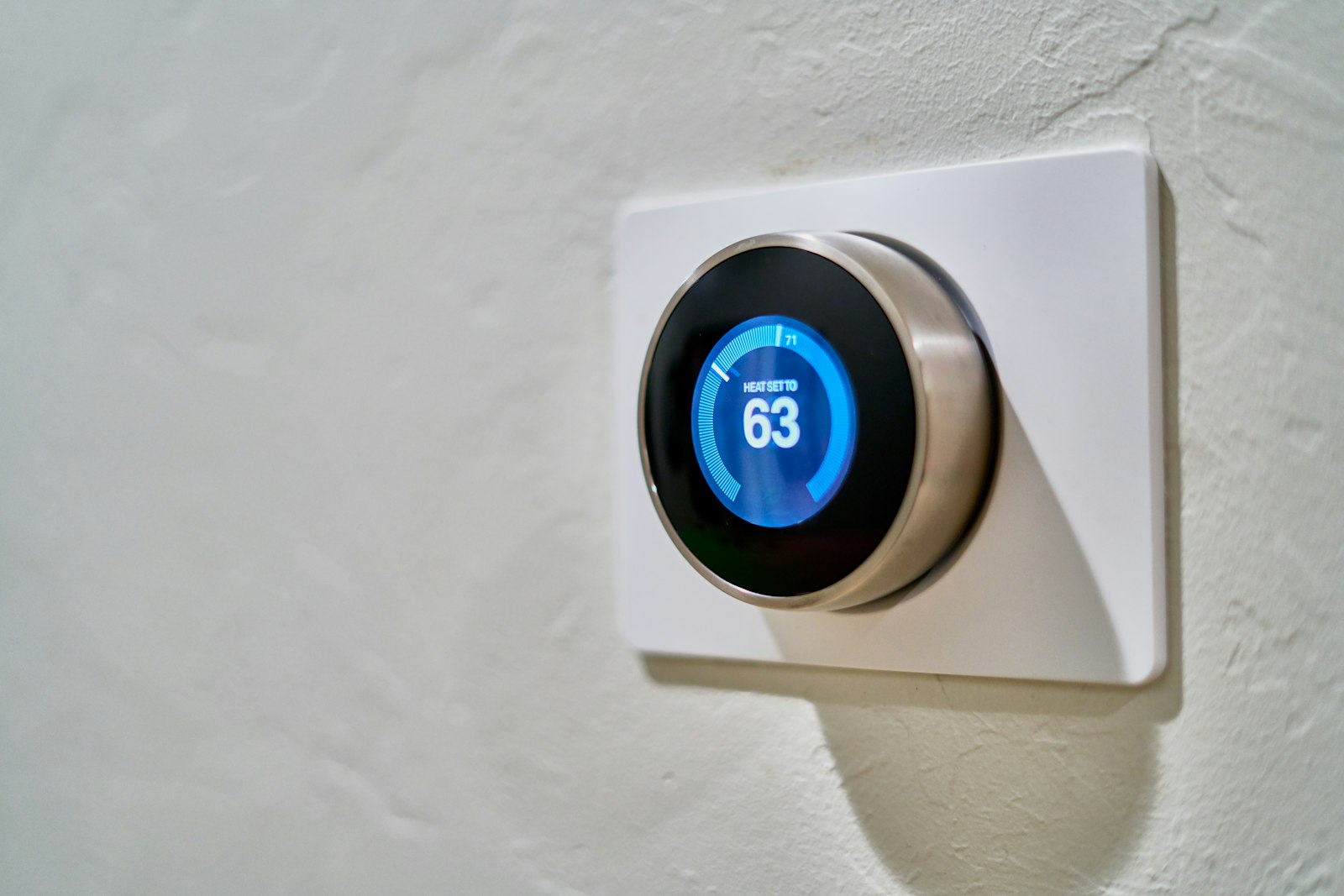 Gray Nest smart thermostat on a wall displaying heat set to 63