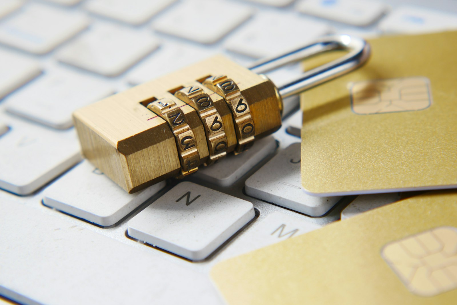 Brass combination padlock resting on a white keyboard beside gold chip cards