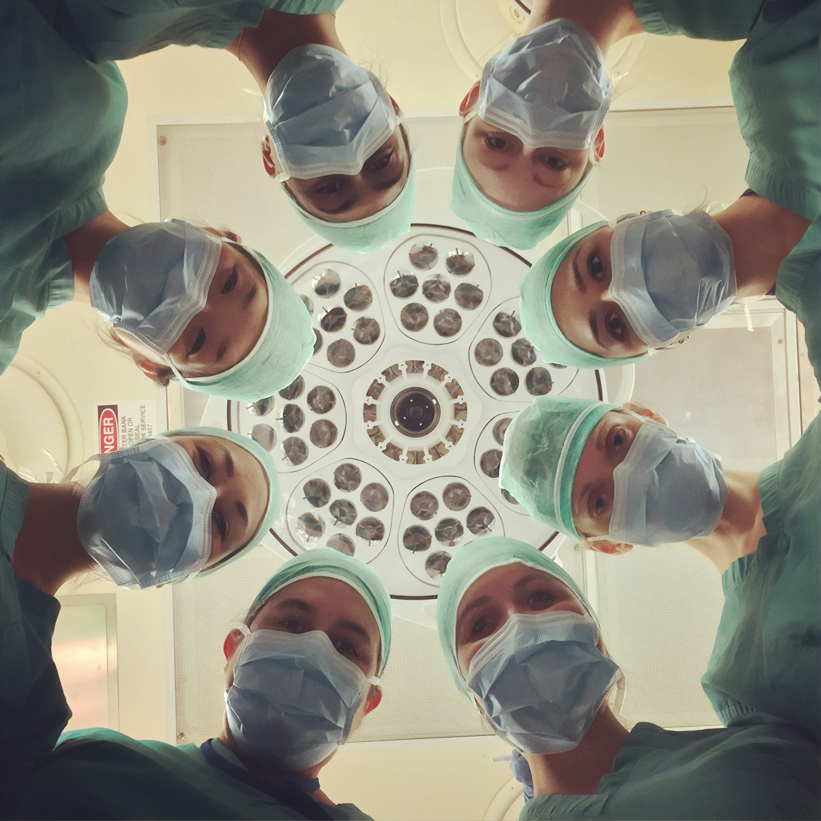 Surgical team in scrubs and masks looking down toward a patient camera angle