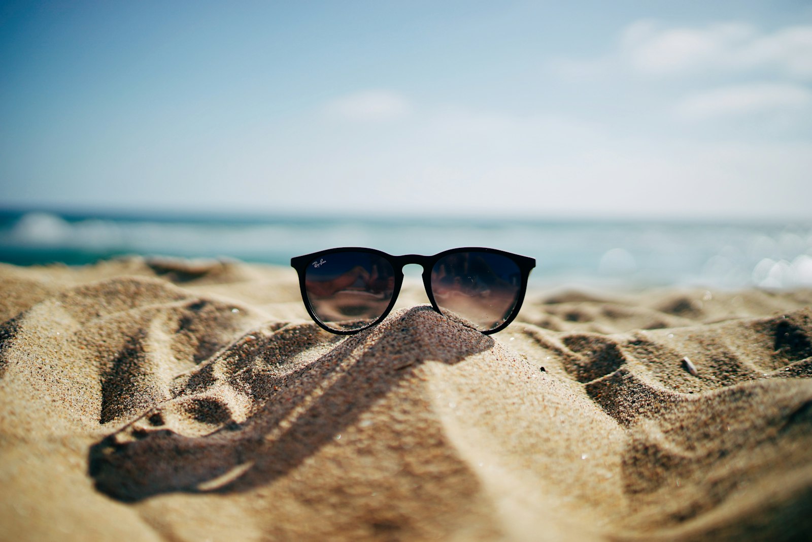 Ray-Ban sunglasses resting in sand on a sunny beach