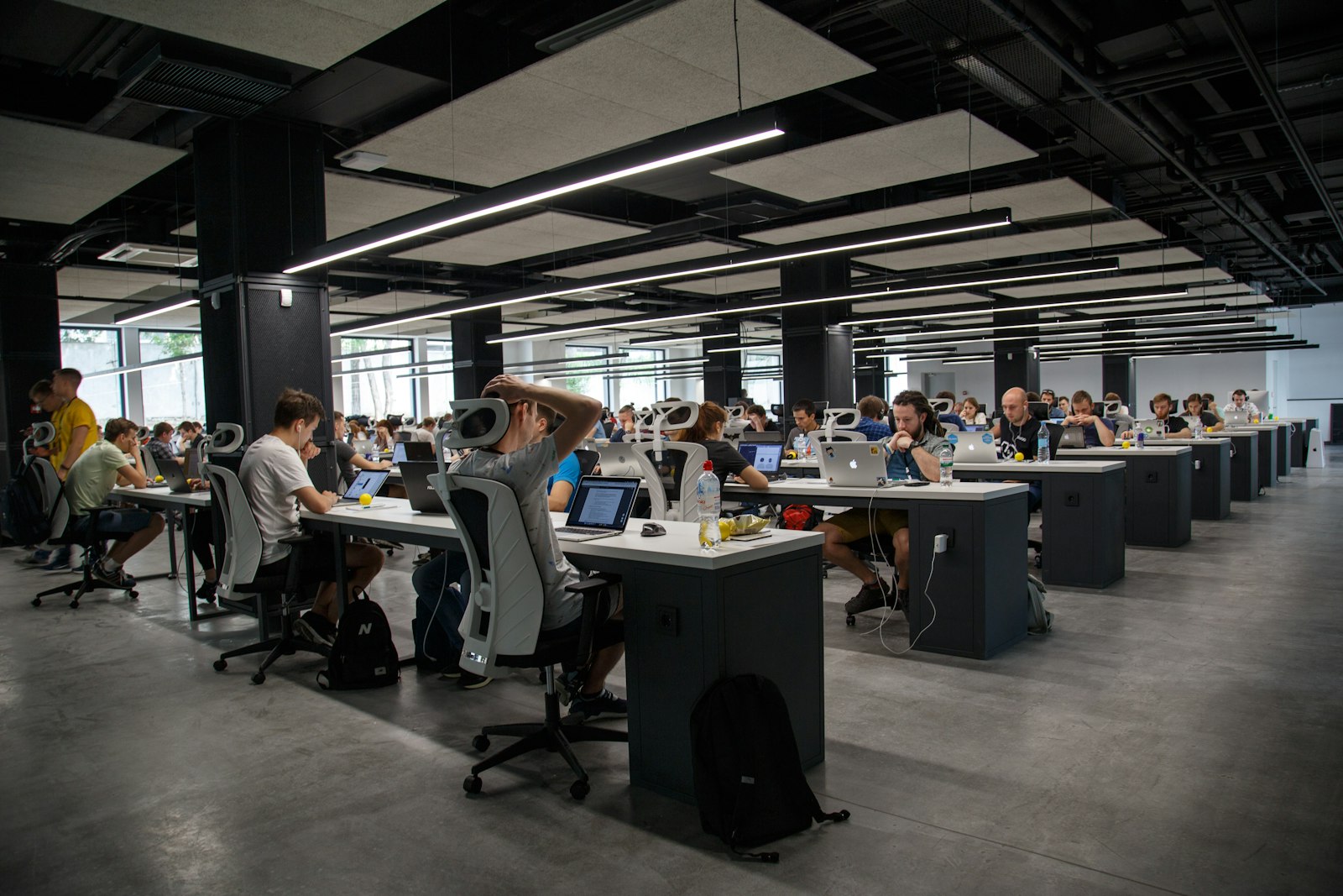 Wide view of a busy open-plan tech office with rows of people working on laptops