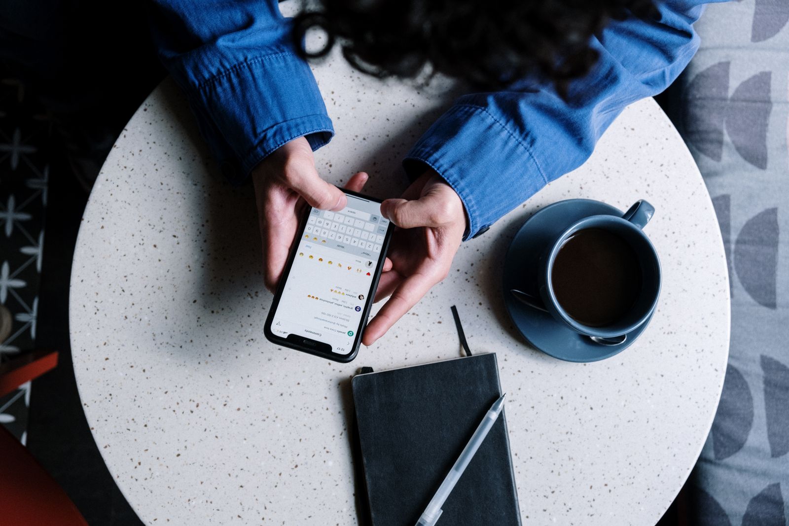 Person typing on a smartphone at a cafe table next to a coffee cup