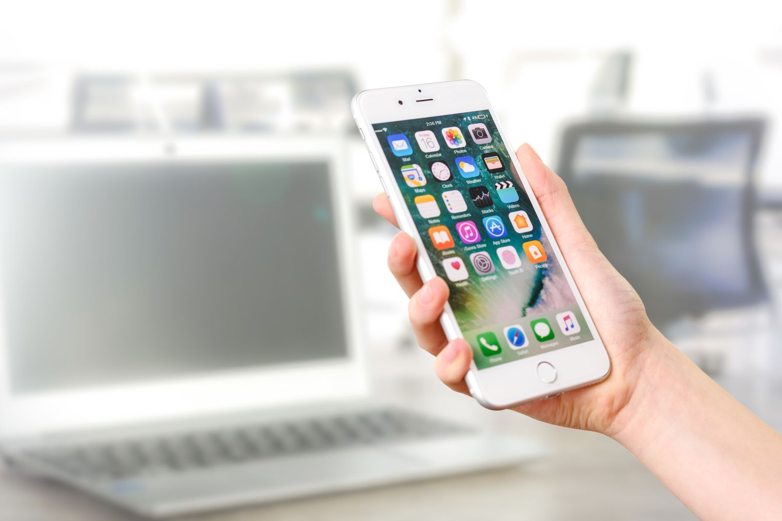 Hand holding a smartphone showing the home screen in an office