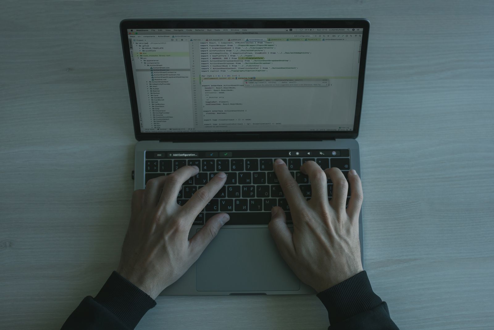 Hands typing on a MacBook laptop showing a code editor