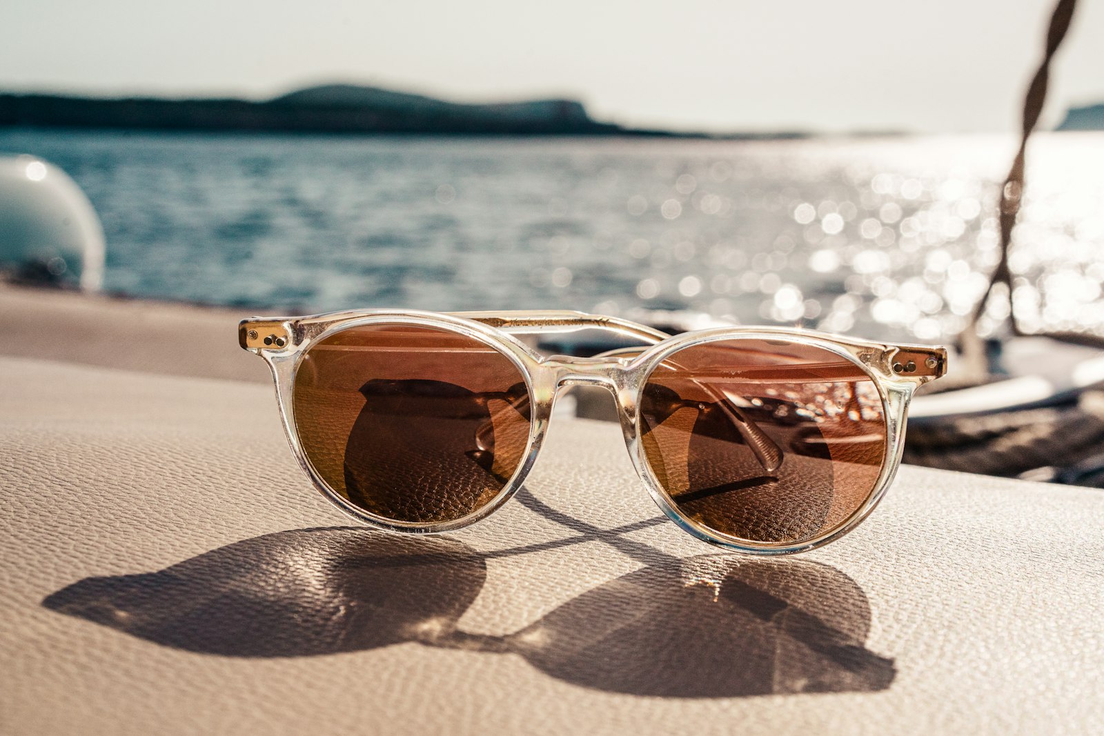 Clear-frame sunglasses resting on a sunlit boat seat by the water