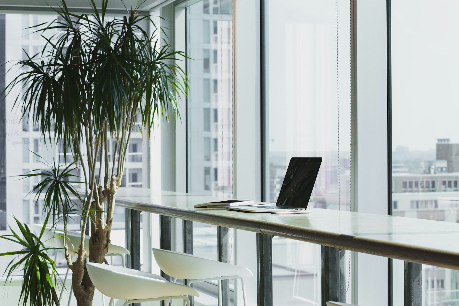 Laptop on a bright office desk by floor-to-ceiling windows